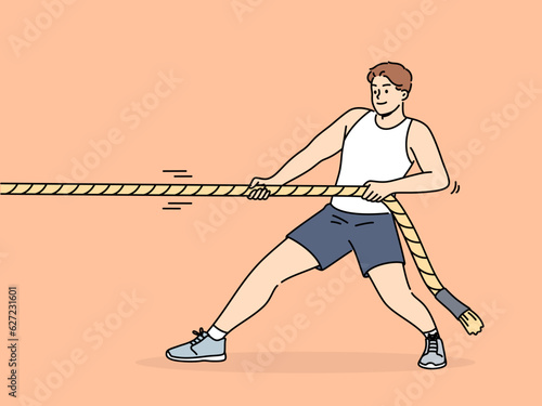 Strong man pulls rope while participating in sports competitions with rivals or training in fitness club. Strongman pulls rope alone, wanting to win tournament and get prize cup or medal.