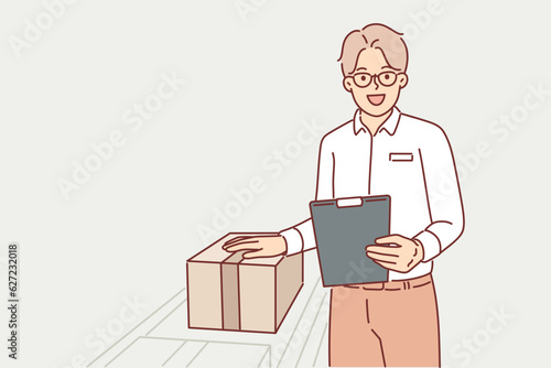 Man warehouse worker stands near conveyor with boxes and holds clipboard checking data on parcels