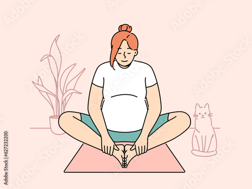 Pregnant woman making morning exercises sitting on fitness mats and getting ready for meditative practices from yoga. Pregnant girl is at home and stretches doing yoga for expectant mothers