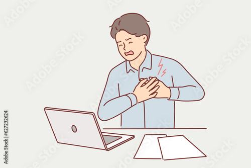Businessman clutching heart feeling pain or infarct doing paperwork sitting at office desk