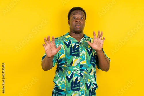 Young latin man wearing hawaiian shirt over yellow background afraid and terrified with fear expression stop gesture with hands, shouting in shock. Panic concept.