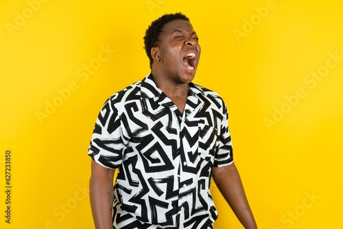 Young latin man wearing printed shirt over yellow background angry and mad screaming frustrated and furious  shouting with anger. Rage and aggressive concept.