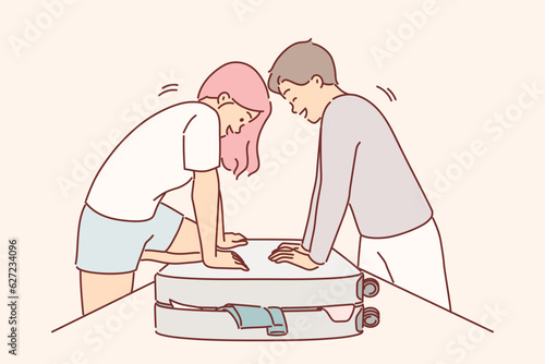 Couple is packing up luggage for travel and trying to close overstuffed suitcase full of clothes