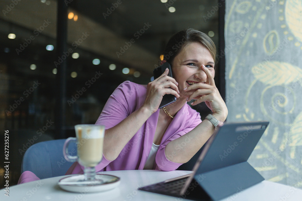 Young caucasian business woman laughing while talking on the phone while sitting in a cafe at a table during lunch. Young caucasian business woman laughing while talking on the phone while sitting in a cafe at a table during lunch.