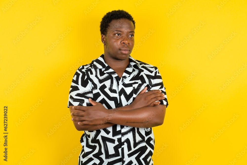 Charming thoughtful Young latin man wearing printed shirt over yellow background stands with arms folded concentrated somewhere with pensive expression thinks what to do Charming thoughtful Young latin man wearing printed shirt over yellow background stands with arms folded concentrated somewhere with pensive expression thinks what to do
