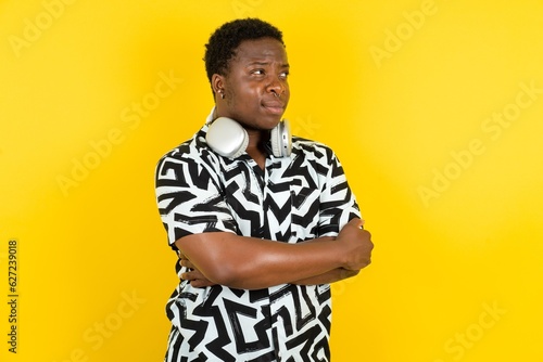 Pleased Young latin man wearing printed shirt over yellow background keeps hands crossed over chest looks happily aside