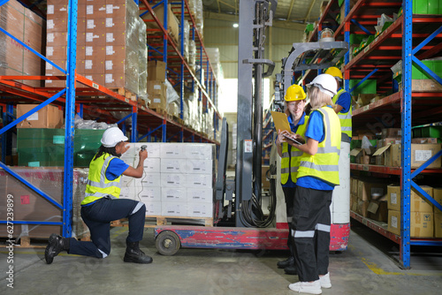 Worker working in large warehouse holding paper chart check list checking the material compare with the boxes wrapped with plastic keep on wooden pallet ready to ship to customer