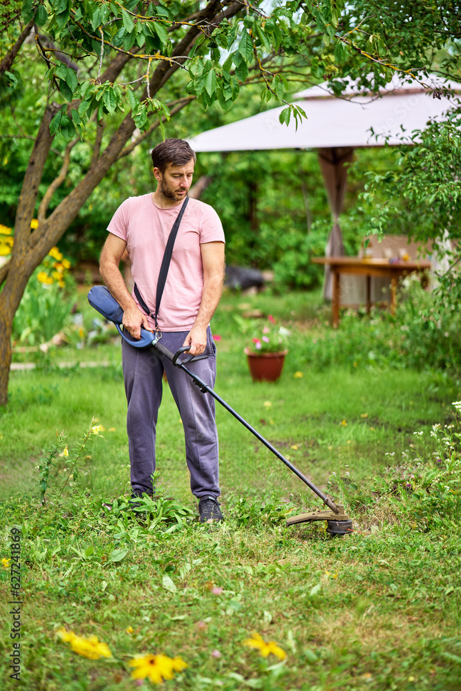 Young man cutting grass with weed cutter on his grassy lawn. Young man cutting grass with weed cutter on his grassy lawn.