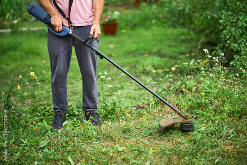 Close up of young man cutting grass with weed cutter on his grassy lawn.