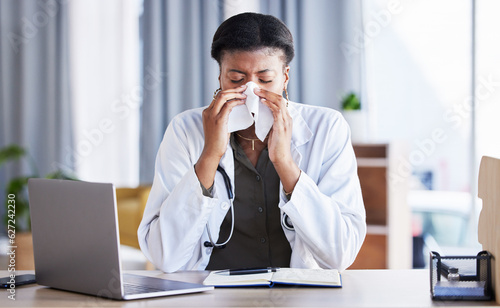 Sick, doctor and a black woman blowing nose in an office as a healthcare employee at a desk. Table, hospital and an African nurse or medical worker sneezing into a tissue with a virus or flu