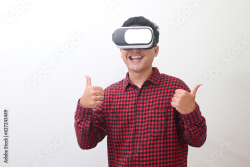 Portrait of Asian man in red plaid shirt using Virtual Reality (VR) glasses and showing thumb up hand gesture. Isolated image with copy space on white background.