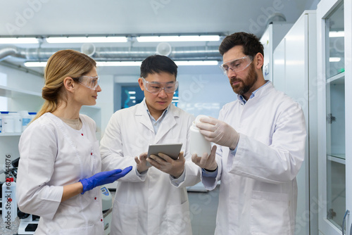 A team of three people, doctors, laboratory workers, scientists are standing inside a laboratory , researchers are communicating and discussing a scientific project, studying research material.
