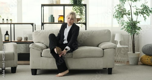 A weary businesswoman lays down on the sofa in the living room. Her tired expression and relaxed posture indicate a need for rest and relaxation after a long day at work. photo