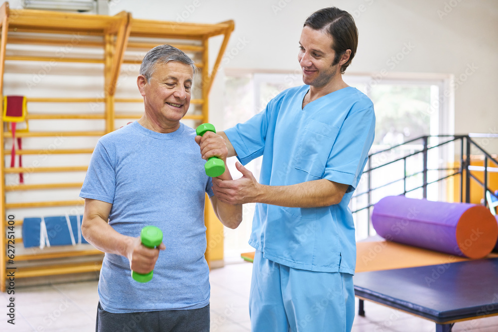 Fototapeta premium Therapist assisting senior man exercising with dumbbells