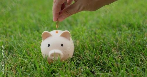 A man puts coins in a piggy bank that stands on a green lawn photo