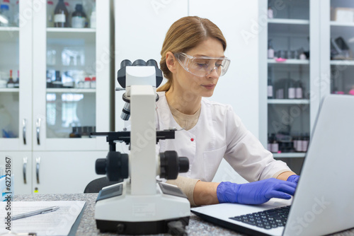Serious and focused female researcher working with microscope inside laboratory, mature and experienced scientist studying and testing medicine.