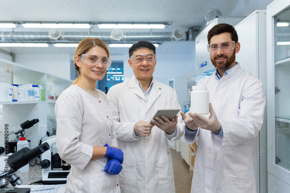 Successful team of scientists, three persons man and woman smiling and looking at the camera, portrait of a group of scientists in white medical coats inside a laboratory. Successful team of scientists, three persons man and woman smiling and looking at the camera, portrait of a group of scientists in white medical coats inside a laboratory.