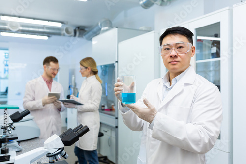 Fototapeta Naklejka Na Ścianę i Meble -  Portrait of an Asian medical scientist, man seriously thinking looking at the camera, laboratory technician working with a team of colleagues researchers.
