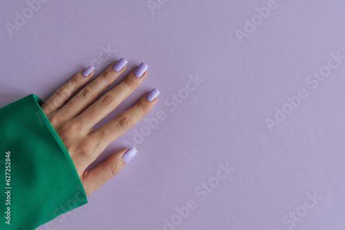 Gelish manicure with purple nails on background of lavender color. Purple fingernails and green clothing