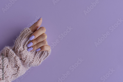 Female's hand with gelish manicure. Nails of trendy lavender color on purple background, copy space photo