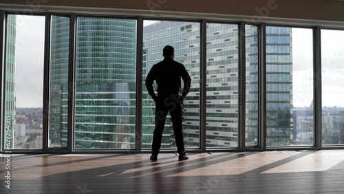 A man in a suit in the office opposite a panoramic window. A confident man approaches the window against the backdrop of skyscrapers. © Ruslan