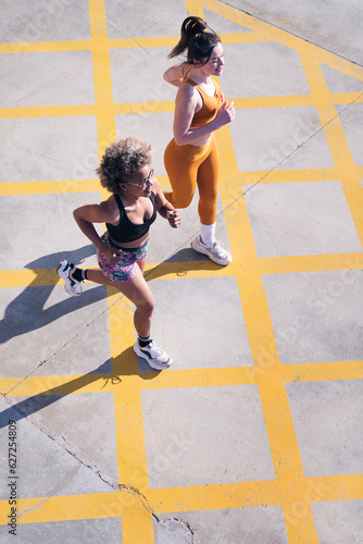 vertical photo of two female friends running happy along city road in a sunny day, concept of friendship and sporty lifestyle, copy space for text