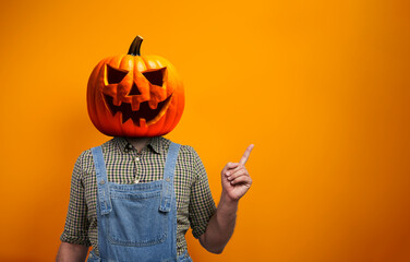 Person in Halloween costume of scarecrow with Jack-o'-lantern pumpkin head points away over orange background with copy space