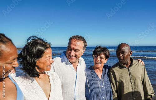 Happy senior people having fun walking on the beach at sunset wearing summer clothes - Joyful elderly lifestyle, vacation and travel concept - Main focus on center friends faces © DisobeyArt