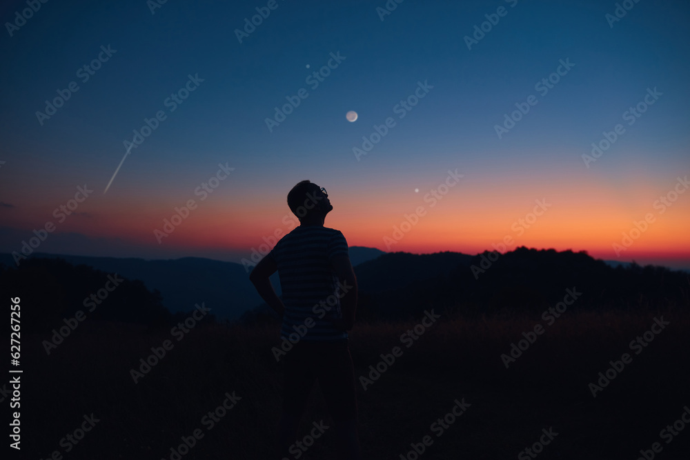 Man looking at the starry skies, crescent Moon and shooting star in blue hour twilight time.