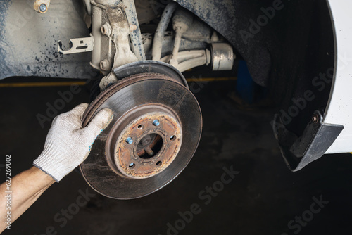 An auto mechanic is engaged in the maintenance of a passenger car in a car workshop, removes an old brake disc to replace it with a new one