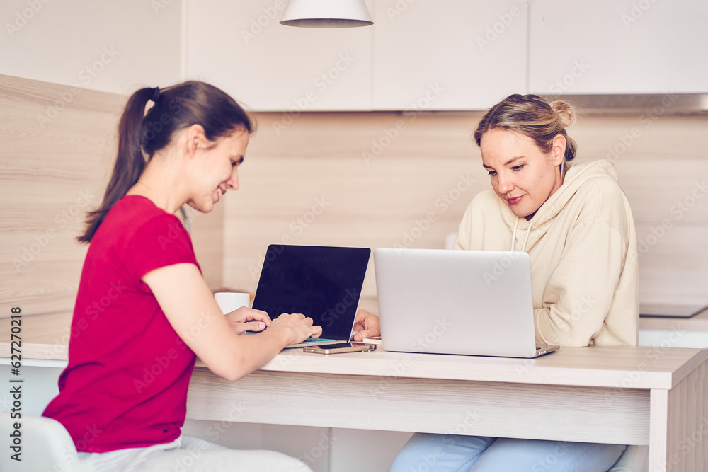 Two happy women using a laptop, work and study online together or make video calls while sitting at a table. Online training. The concept of a career of a female entrepreneur. High quality photo Two happy women using a laptop, work and study online together or make video calls while sitting at a table. Online training. The concept of a career of a female entrepreneur. High quality photo
