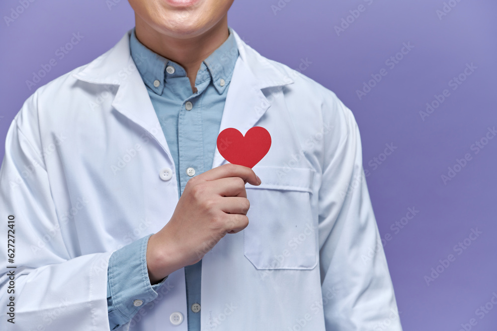 Φωτογραφία Portrait of confident young male doctor holding heart over purple background