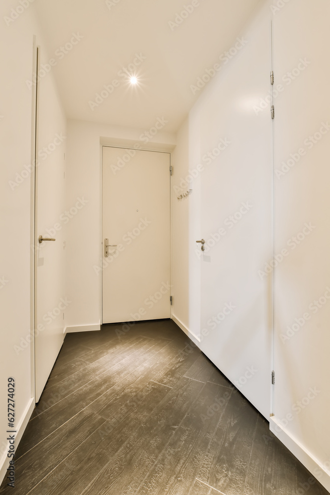 an empty room with white walls and wood flooring on the right, there is a door to the left an empty room with white walls and wood flooring on the right, there is a door to the left