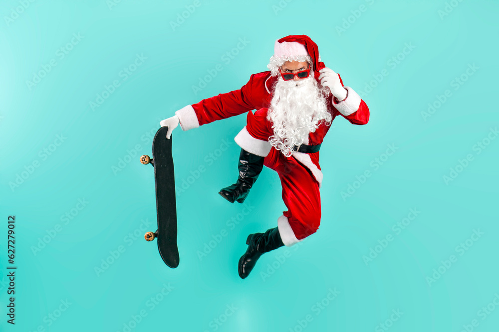 santa claus in sunglasses and suit jumps and flies with skateboard on blue isolated background santa claus in sunglasses and suit jumps and flies with skateboard on blue isolated background