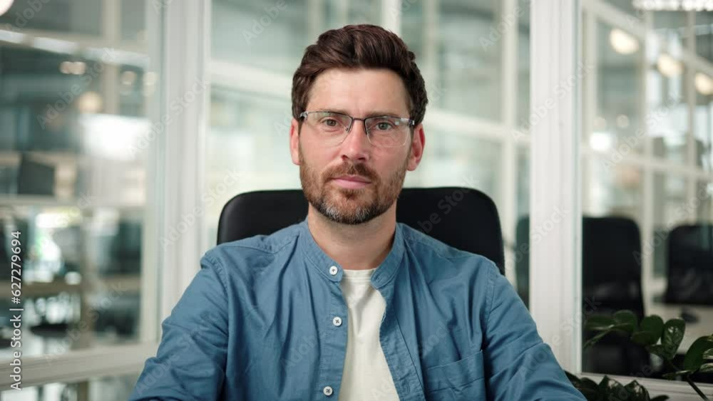 Handsome businessman, lawyer, or attorney in a blue shirt adjusts his glasses and confidently smiles at the camera, showing friendliness and openness to collaboration. The man is in a modern office. Handsome businessman, lawyer, or attorney in a blue shirt adjusts his glasses and confidently smiles at the camera, showing friendliness and openness to collaboration. The man is in a modern office.