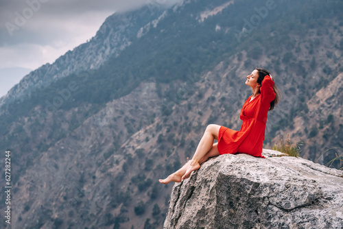 Romantic photo of a girl in a red dress on top of a cliff admiring the view of a mountain gorge © EdNurg