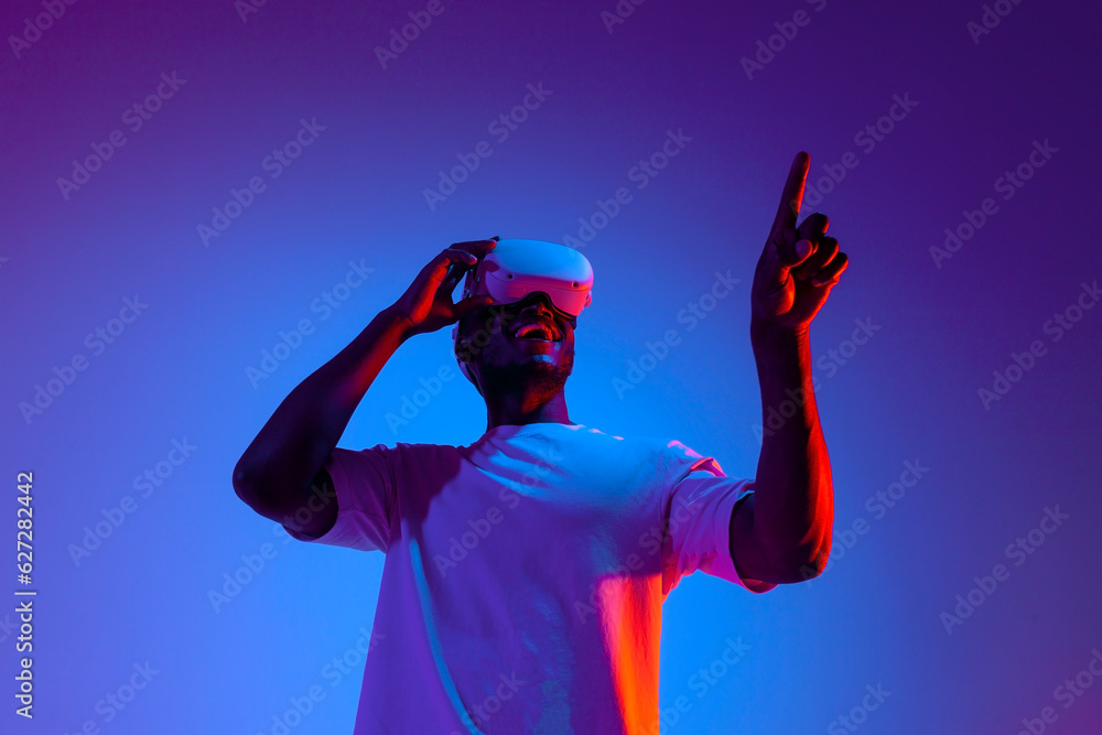 african american male gamer in virtual reality glasses touches his hands in neon lighting african american male gamer in virtual reality glasses touches his hands in neon lighting