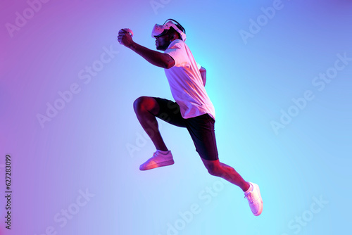 african american athletic man jumping in virtual reality glasses in neon lighting, the guy athlete runs and trains © Богдан Маліцький