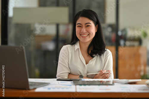 Portrait image of Young Asian businesswoman smiling and crossing her arms confidently while looking at the camera.