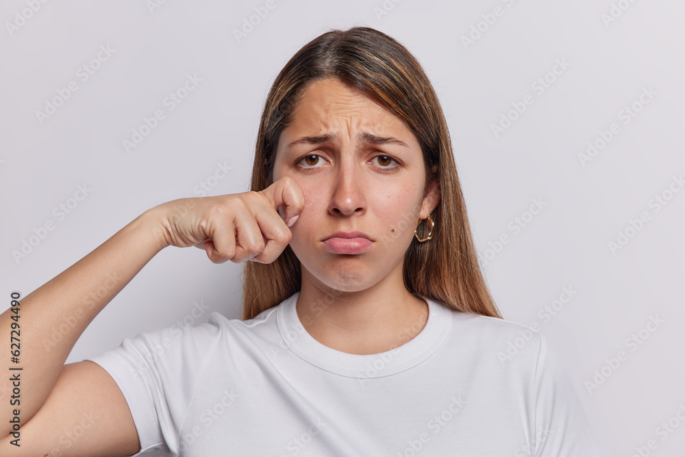 Upset doleful young woman breaks down in sobs and cries of despair wipes away her tears finding solace in grief frowns face dressed in casual t shirt isolated over white background. Negative emotions Upset doleful young woman breaks down in sobs and cries of despair wipes away her tears finding solace in grief frowns face dressed in casual t shirt isolated over white background. Negative emotions