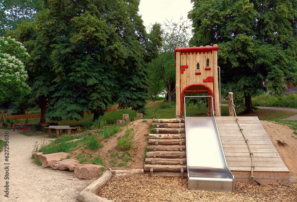 Spielgerät auf Spielplatz aus Holz mit Holzhaus und Rutsche in einem Park in grüner Natur. Spielgerät auf Spielplatz aus Holz mit Holzhaus und Rutsche in einem Park in grüner Natur.