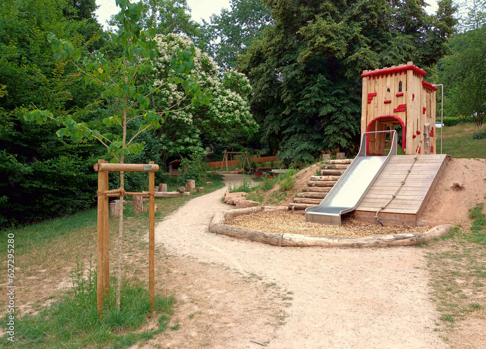 Spielgerät auf Spielplatz aus Holz mit Holzhaus und Rutsche in einem Park in grüner Natur. Spielgerät auf Spielplatz aus Holz mit Holzhaus und Rutsche in einem Park in grüner Natur.