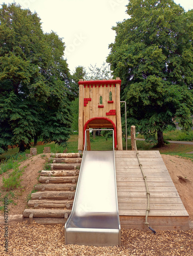 Spielgerät auf Spielplatz aus Holz mit Holzhaus und Rutsche in einem Park in grüner Natur.  photo