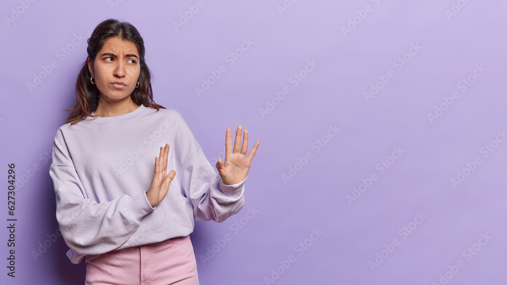 Serious young Iranian woman extends her palms to side signaes to keep distance and not come closer emphasizes importance of maintaining personal space. Self preservation social distancing concept Serious young Iranian woman extends her palms to side signaes to keep distance and not come closer emphasizes importance of maintaining personal space. Self preservation social distancing concept