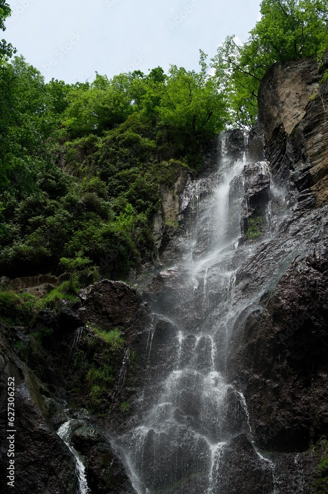 Fototapeta premium A small high and powerful waterfall tumbles down a turbulent stream.