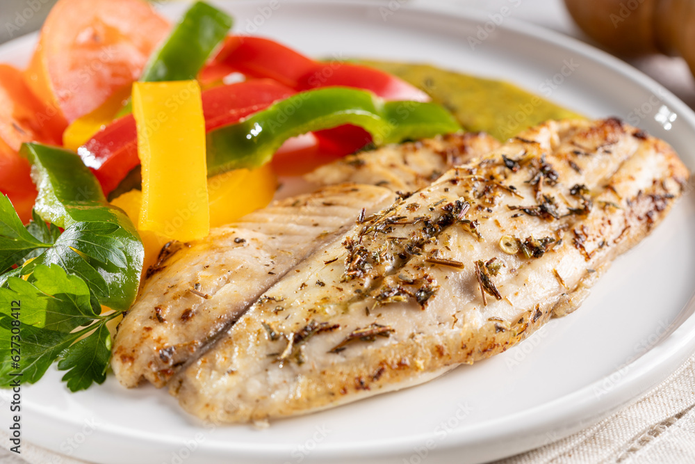 Grilled tilapia fillet with spices and colored peppers.