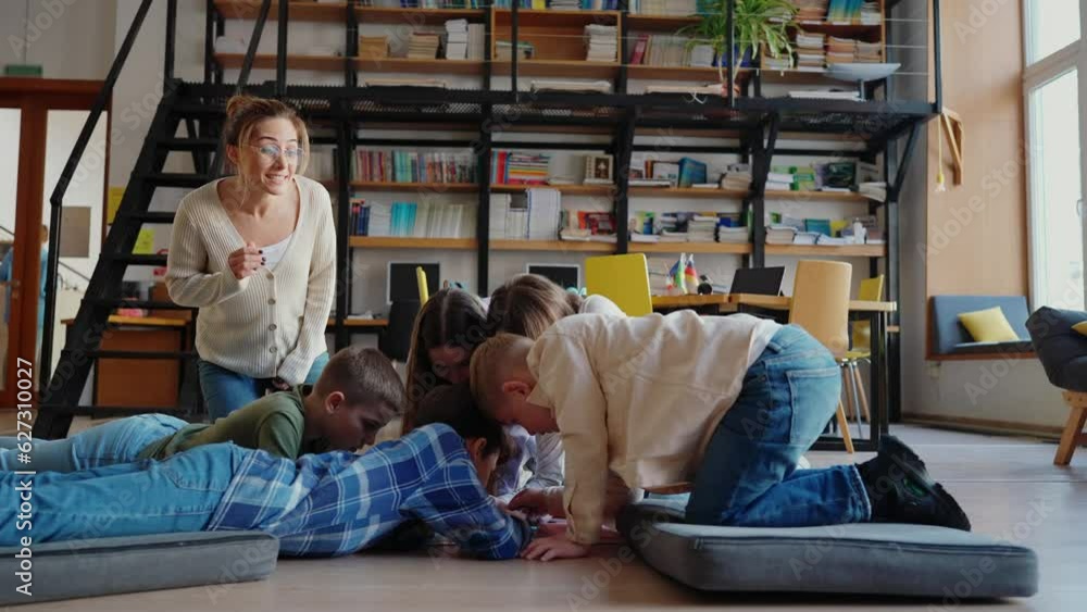 Handsome children and their teacher look at map of world sitting on floor in library Handsome children and their teacher look at map of world sitting on floor in library