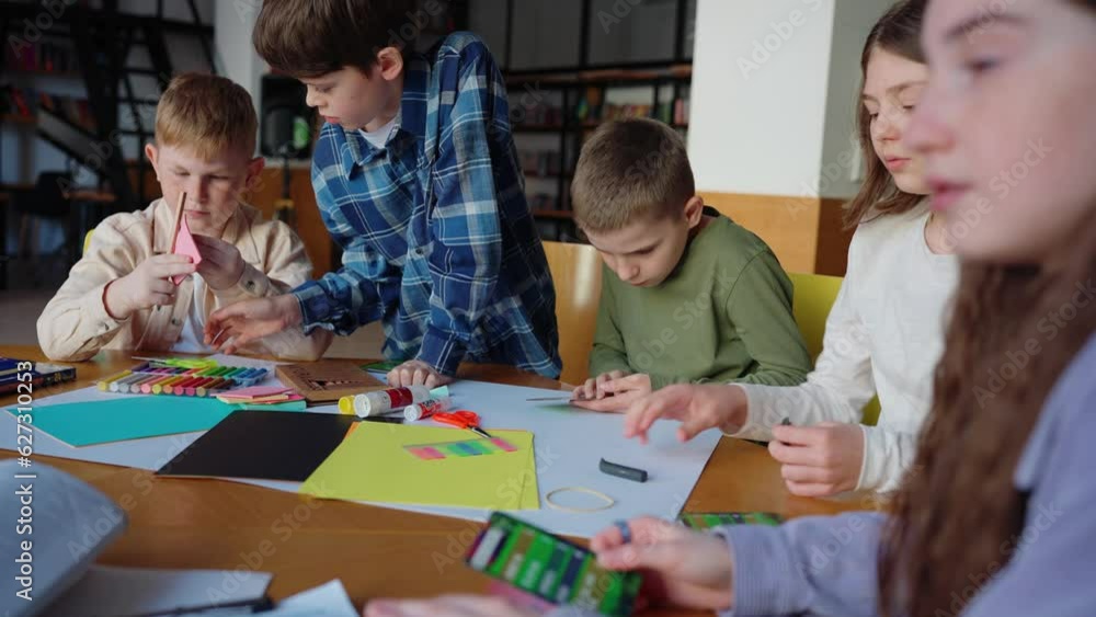 Concentrated children drawing with crayons and preparing to make origami at table at library Concentrated children drawing with crayons and preparing to make origami at table at library