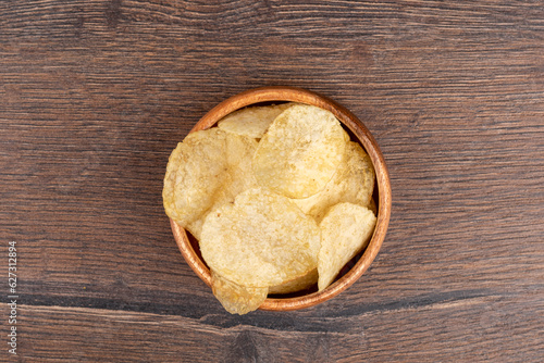 Top view. Potato chips in a wooden bowl are good for beer or ale snacks on a dark wooden table.