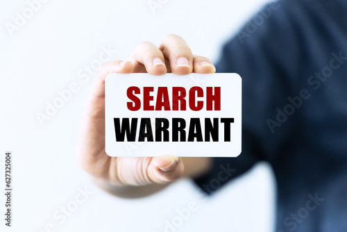 Search warrant text on blank business card being held by a woman's hand with blurred background. Business concept about search warrant.